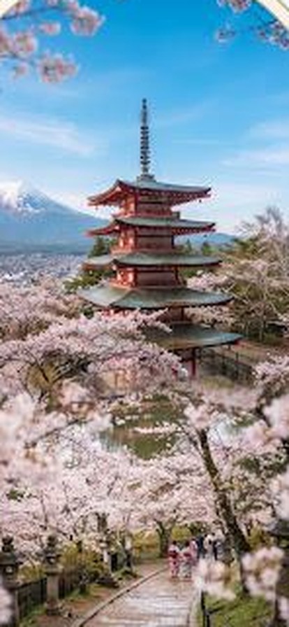 A red pagoda framed by cherry blossom with Mount Fuji rising behind it